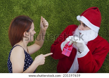 Angry portrait of a young woman holding fist and pointing with a finger to a gift and afraid young man portrait wearing santa costume isolated on green background.Disappointment concept.