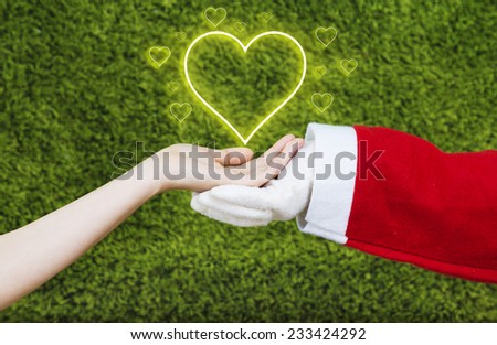 Santa Claus hand in white glove holding together with a woman hand  little hearts surrounding a big heart isolated on green background.