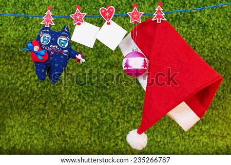 Christmas decoration santa hat and a cat toy and empty two sheet of paper with a red ribbon hanging on rope over green  background