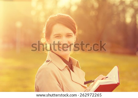 Young smiling businesswoman,student professional outdoors  holding a red ,journal writing in it.Businesswoman smiling,Life style,