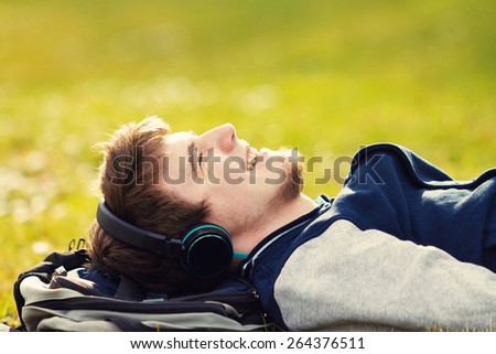 Young student, man relaxing smiling while lying on grass and listening to music.Player.Music,Relax