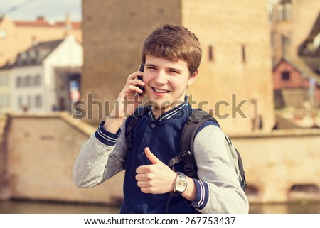 Smiling young man talking on mobile phone in a city with thumb up .Young smiling student  outdoors talking on cell smart phone.Life style.City