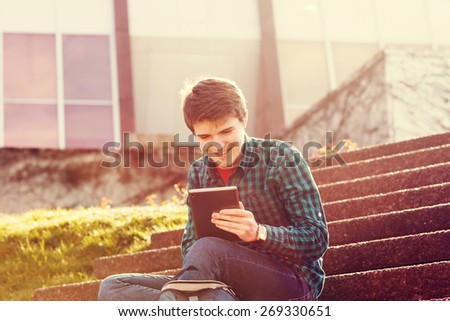 Smiling young man taping on tablet in a city on stair .Young smiling student  outdoors  with tablet.Life style.City