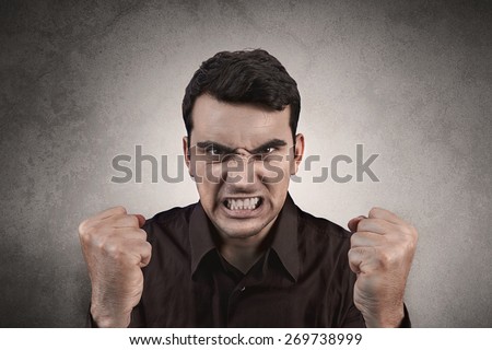 Stressed, aggressive, frustrated portrait of a young student, man,screaming holding his fists up isolated on black background.Facial expression