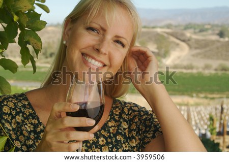 Beautiful smiling woman at a country winery tasting wine on a summer day.
