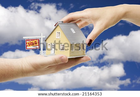 Reaching For A Home with Sold Real Estate Sign on a Bright Blue Cloudy Sky Background.