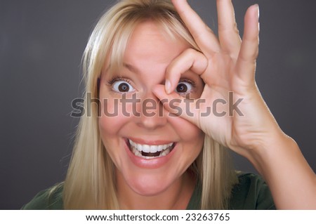 Woman with Okay Sign in Front of Face Against a Grey Background.