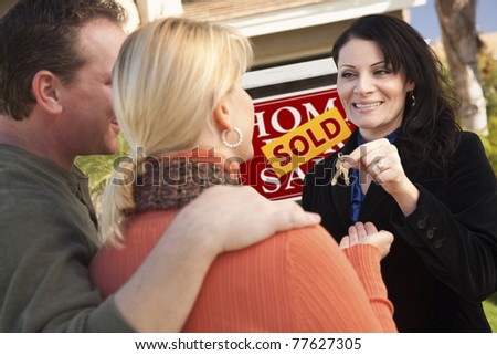 Attractive Hispanic Female Real Estate Agent Handing Over New House Keys to Happy Couple.