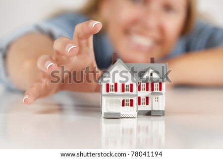 Smiling Woman Reaching for Model House on a White Surface.