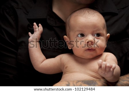 Young Father with Tattoo Holding His Mixed Race Newborn Baby Under Dramatic Lighting.