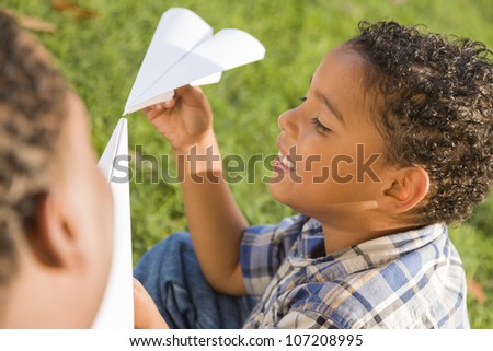 Happy Mixed Race Father and Son Playing with Paper Airplanes in the Park.