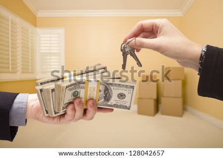 man and Woman Handing Over Cash For House Keys Inside Empty Room with Boxes.
