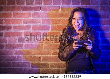 Portrait of a Pretty Mixed Race Young Adult Woman Using Her Cell Phone Against a Brick Wall with Plenty of Copy Space.
