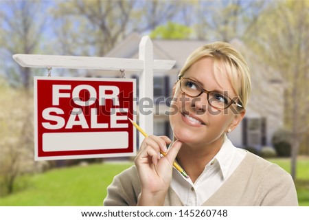 Attractive Young Adult Woman with Pencil in Front of For Sale Real Estate Sign and House.