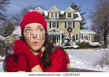Smiling Mixed Race Woman Looking To The Side in Winter Clothing Outside of Decorated House in the Snow.