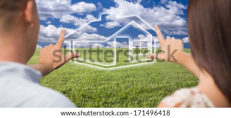 Dreaming Couple Framing Hands Around Ghosted House Figure in Grass Field.