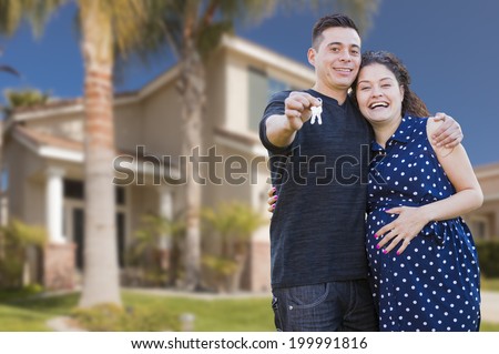 Happy Hispanic Couple In Front of New Home Showing Off Their House Keys.