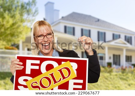 Excited Woman Holding House Keys and Sold Real Estate Sign in Front of Nice New Home.