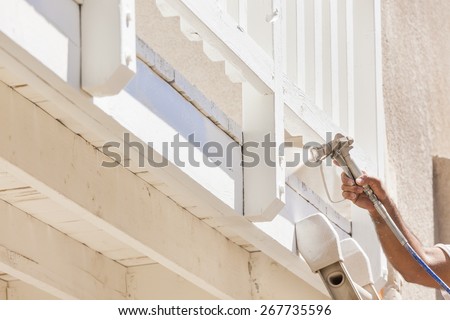House Painter Wearing Facial Protection Spray Painting A Deck of A Home.