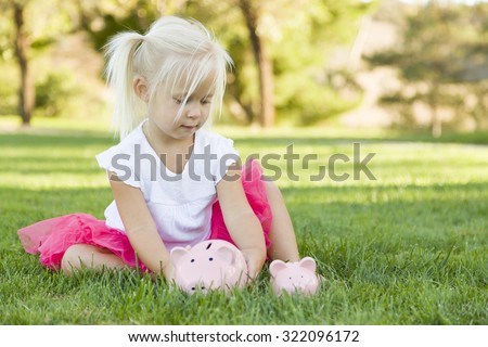 Cute Little Girl Having Fun with Her Large and Small Piggy Banks Outside on the Grass.