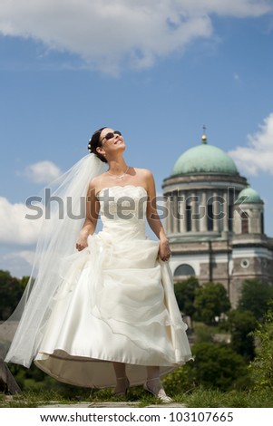 Attractive young bride enjoy sunshine against church and blue sky.