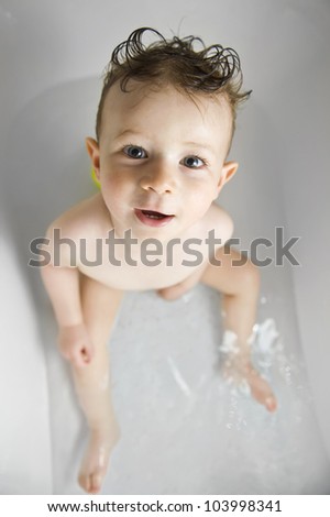 Cute baby boy with funny hair bath in the bathtub looking at the camera.