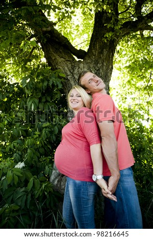 Portrait of a happy pregnant couple in jeans and pink t-shirts standing back to back.