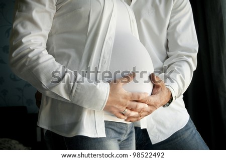Man and woman\'s hands overÃ?Â pregnant belly on black in white shirt.