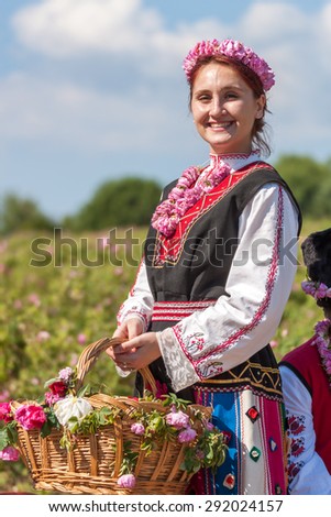Woman dressed in a Bulgarian traditional folklore costume picking roses in a garden, as part of the summer regional ritual in Rose valley, Bulgaria.