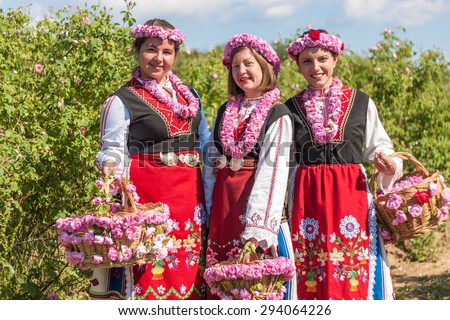 Women dressed in a Bulgarian traditional folklore costume picking roses in a garden, as part of the summer regional ritual in Rose valley, Bulgaria.