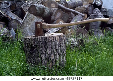 An axe stuck in a log in front of a pile of wood
