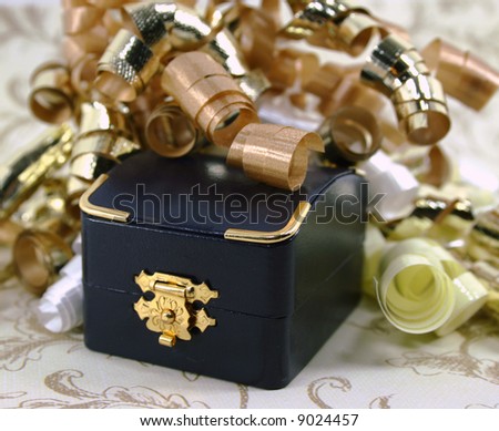 A small closed navy blue jewelry box surrounded by curly gold, white and yellow ribbon.