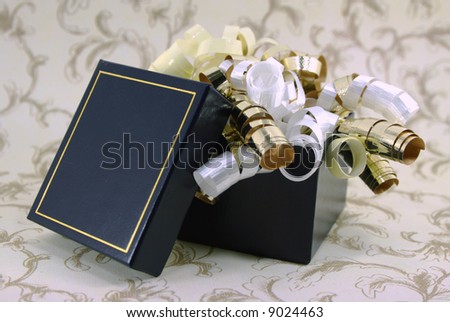 Curly gold, white and yellow ribbons spill out of a navy blue gift box.