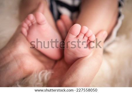 Baby\'s feet in mother\'s hand. newborn baby feet on female hands. Baby feet on white coverlet. Toes. Feet how a heart or \