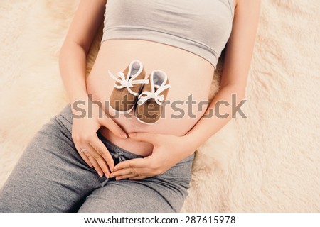 Closeup of pregnant woman holding her hands on her swollen belly shaping a heart, toned retro or instagram effect.