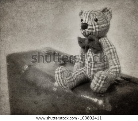 Vintage-style teddy bear and old suitcase with textured blackground