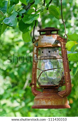 Picturesque old rustic oil lantern hanging in an apple tree with green foliage background