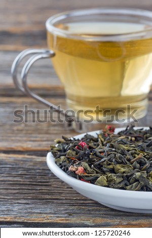 Green tea leaves on a plate, glass cup of tea in the background