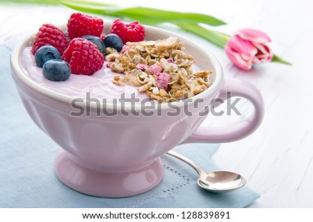 Berries and yoghurt in pink elegant cup with cereal granola, pink tulip in background