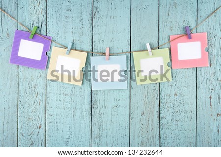 Five empty colorful photo frames or notes paper hanging with clothespins on wooden blue vintage shabby chic background