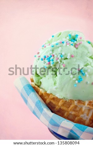 Green pear ice cream in a cone on vintage pink textured background