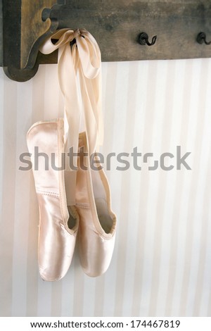 Cream color ballet pointe shoes hanging from wooden rack with striped wallpaper for copy space
