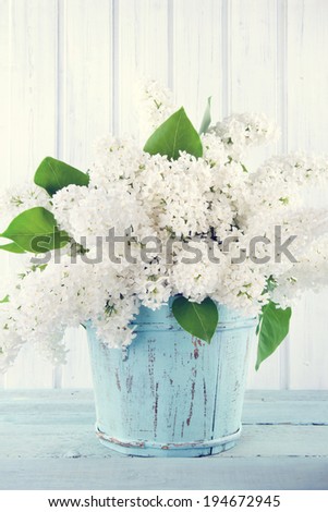 Bouquet of white lilac flowers in a wooden blue vase on light shabby chic background
