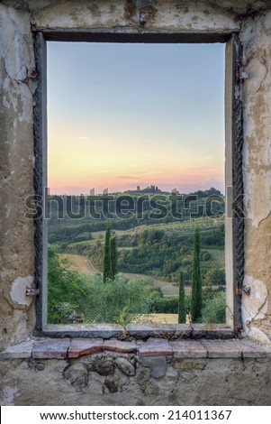 Framed view from an old window in an abandoned stone house to a green Tuscany landscape wit hills and cypresses