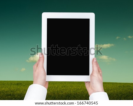 Tablet hand held in a vertical position against the background of meadows and sky