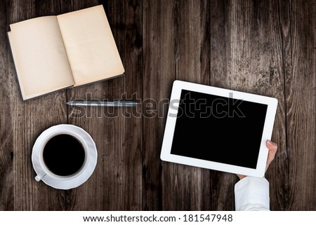 Woman holding hands of a tablet with blank screen on a wooden table coffee book's pen