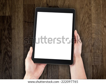 woman\'s hand holding a tablet on the background of a wooden tabletop