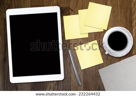 Digital tablet computer with sticky note paper and cup of coffee on old wooden desk. Simple workspace or coffee break with use of web .