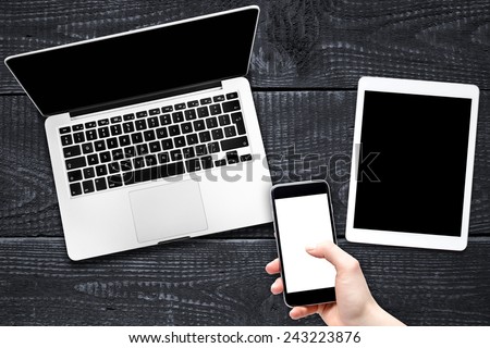 Open laptop with digital tablet and smartphone in hand. All with isolated screen on old wooden desk.