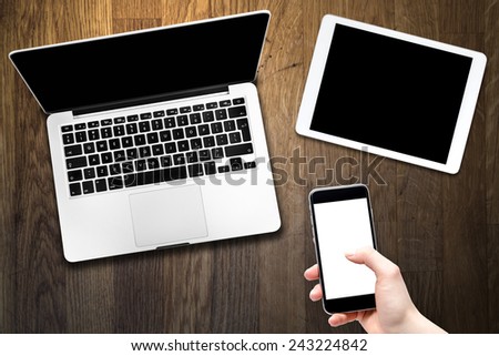 Open laptop with digital tablet and smartphone in hand. All with isolated screen on old wooden desk.